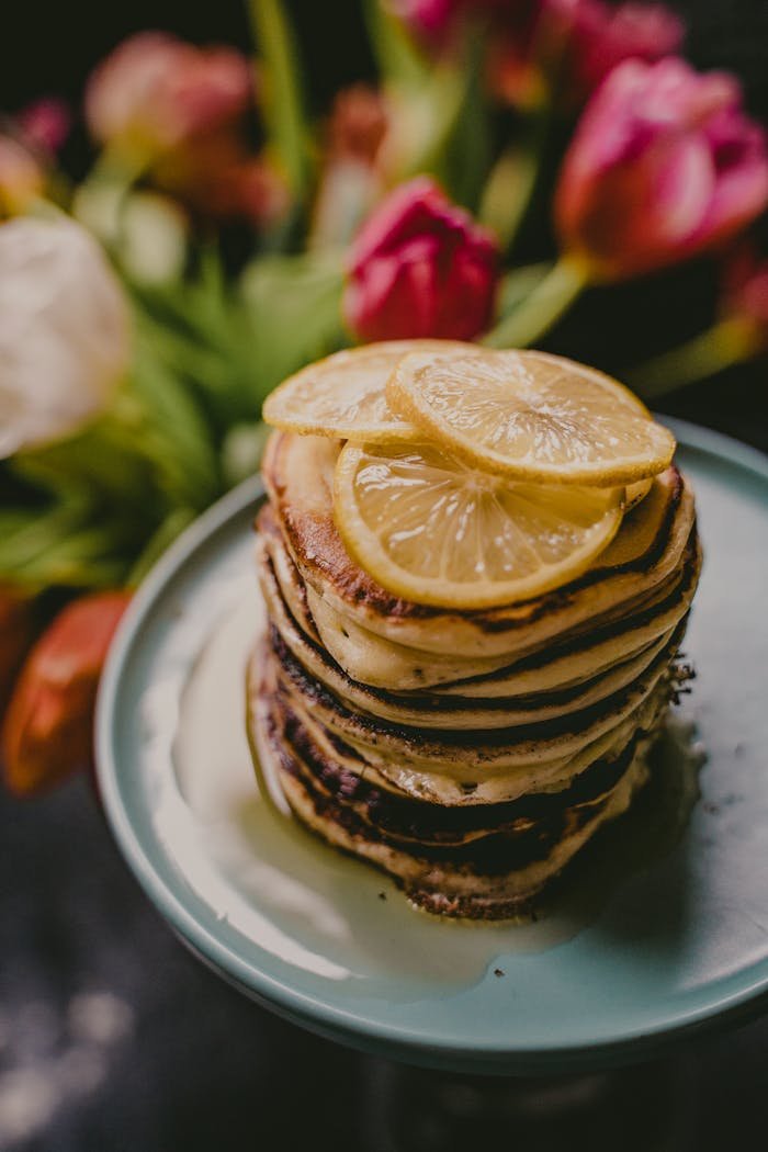 Delicious lemon pancakes stacked on a plate, with vibrant tulips in the background.